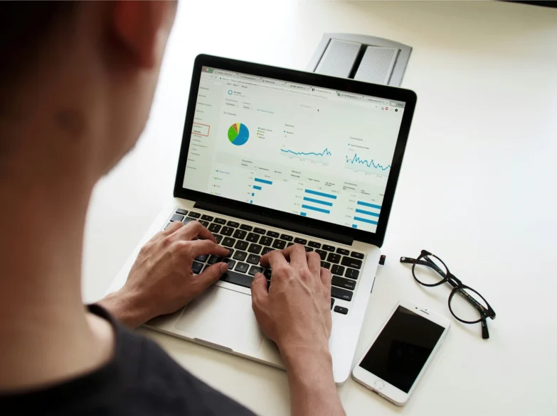 A person types on a laptop displaying a colorful graph, focused on their work.