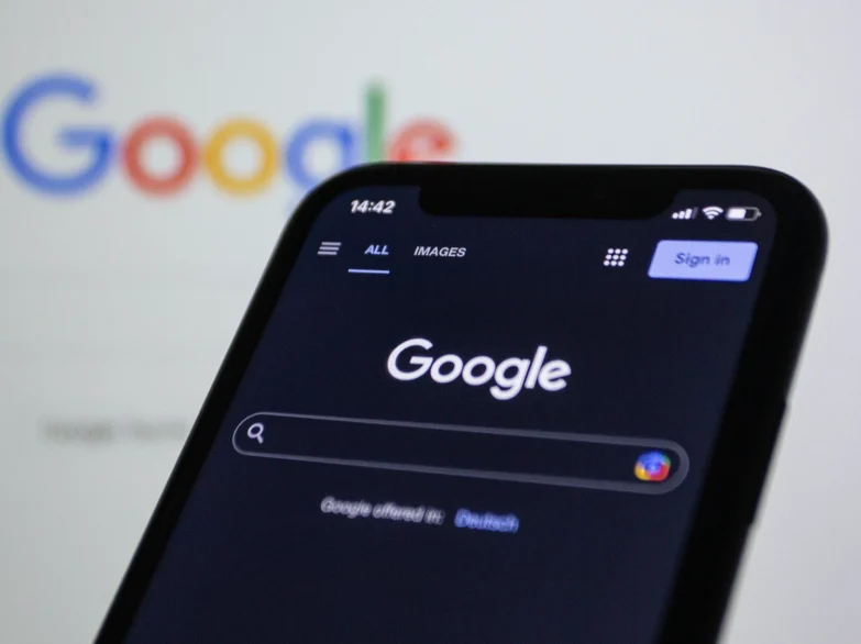 Google on a mobile device in font of a laptop screen.