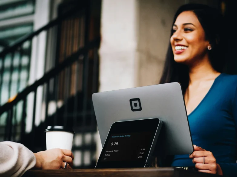 A woman smiling at a customer who is holding a coffee.