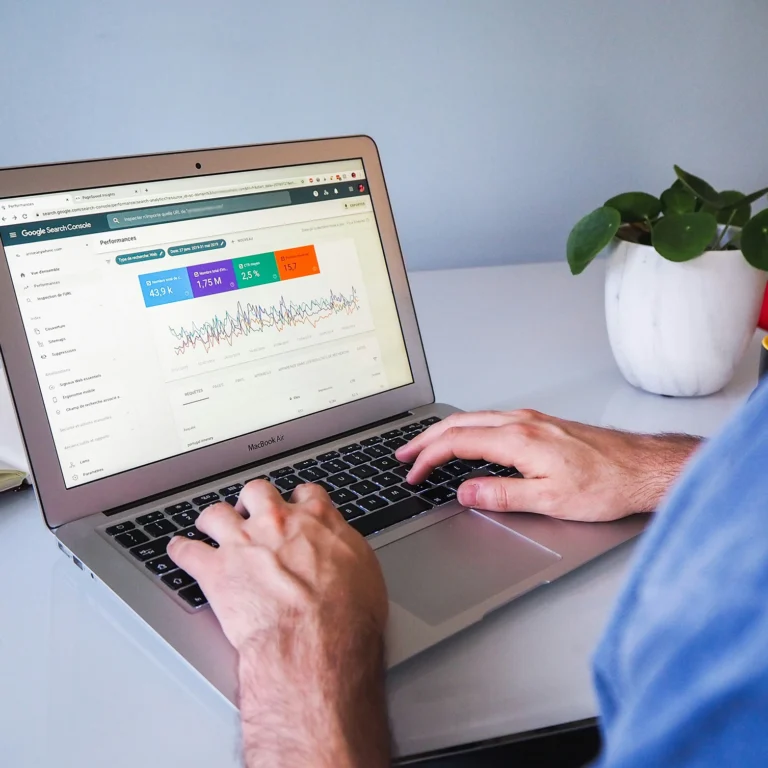 A person working on a laptop displaying a colourful Google Console graph, focused on data analysis.